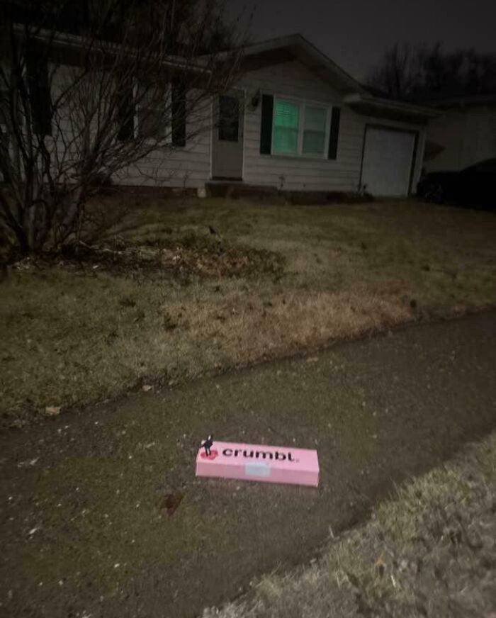 Pink Crumbl delivery package dropped off track on a dark suburban sidewalk, illustrating package delivery mishaps.