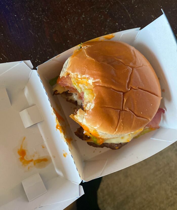 Partially eaten burger in a delivery box with sauce stains, illustrating a delivery that went totally off track.
