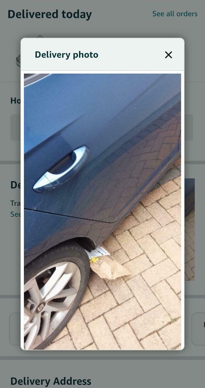 Package delivery mistakenly placed under car tire on a paved driveway, showing a common example of deliveries gone off track.