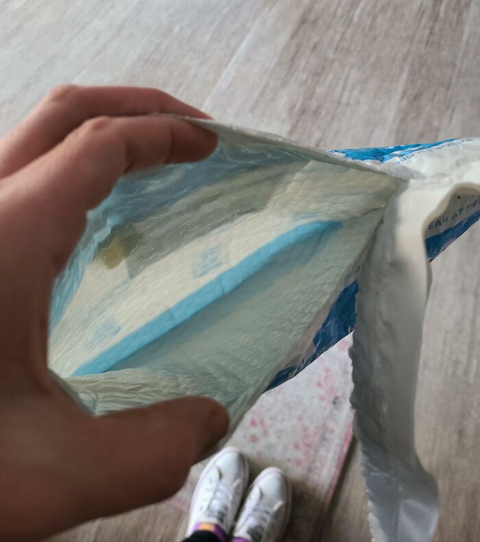Hand holding an empty blue and white package mailer bag with visible interior and white sneakers on floor below.