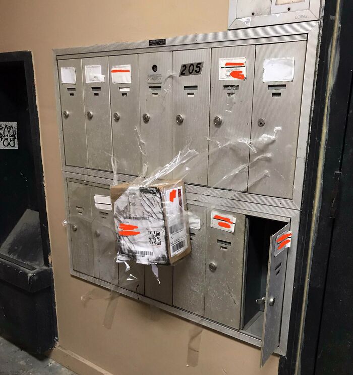 Damaged package taped awkwardly to a mailbox unit with one mailbox door left open, showcasing delivery mishap and tracking issues.