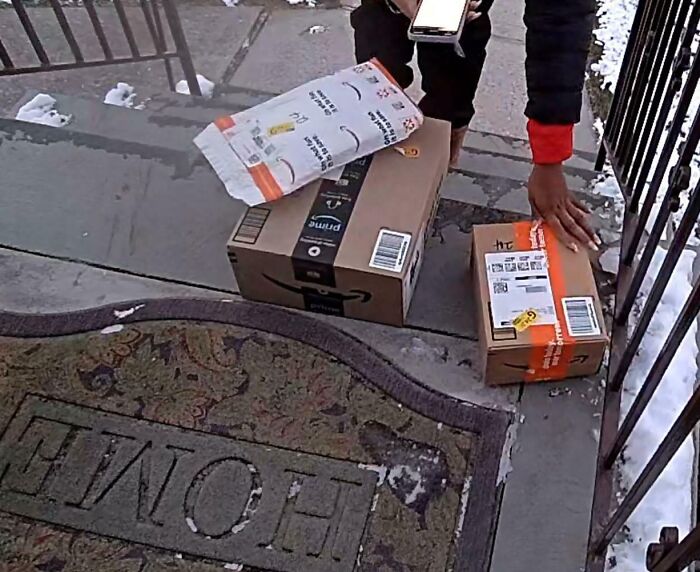 Person placing Amazon packages on a snowy doorstep near a home entrance during a delivery outside.