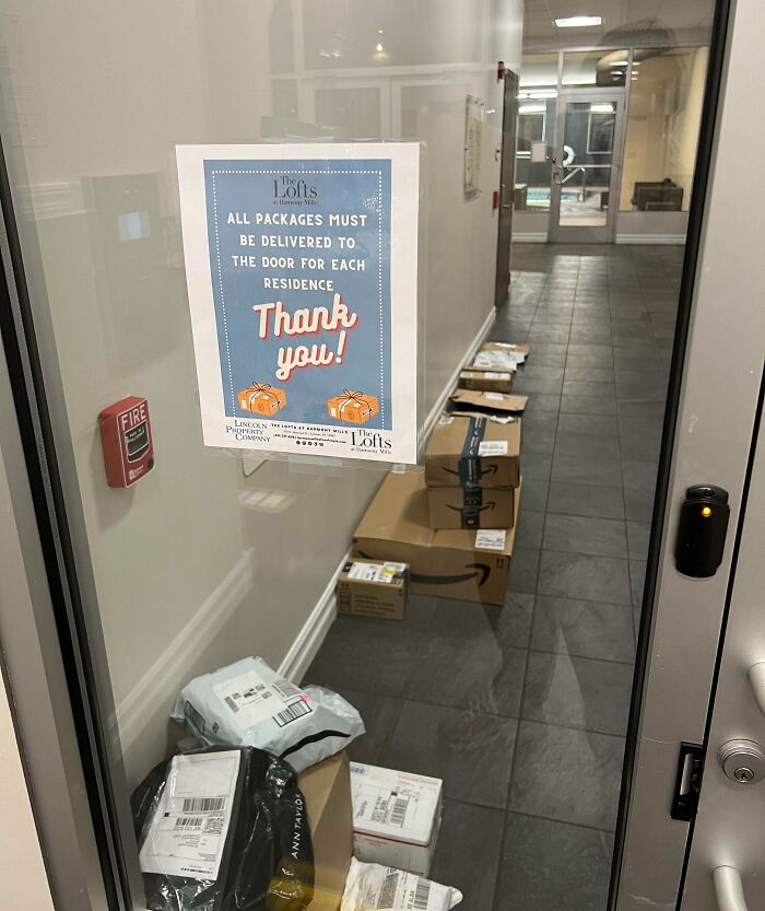 Packages piled inside apartment hallway despite sign requiring delivery to resident doors, showing delivery failures and off track packages.