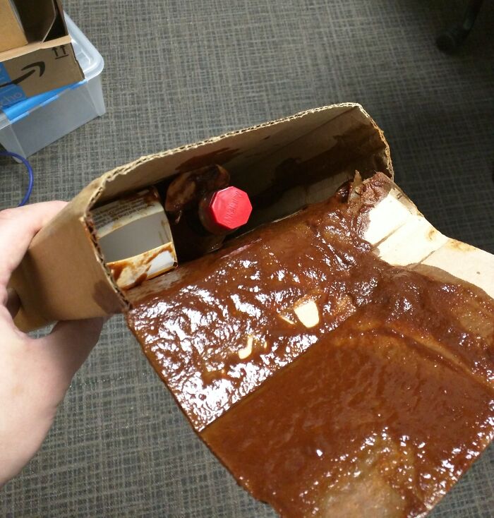 Damaged delivery package leaking sauce inside a soggy cardboard box, showing an unfortunate delivery gone off track.