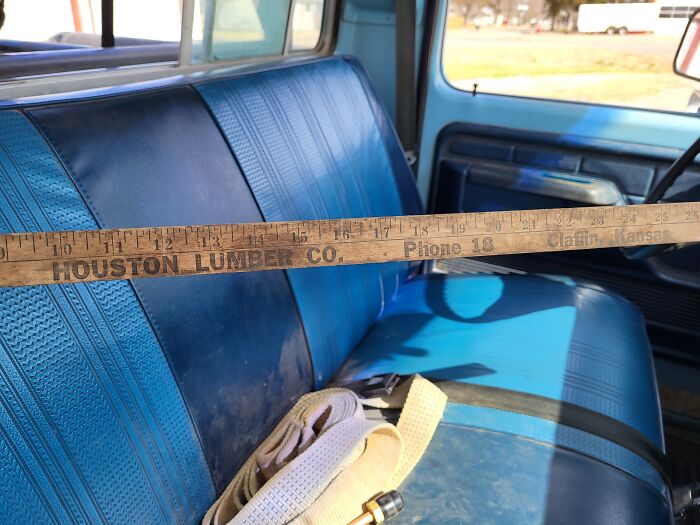 Vintage 1950s truck interior with blue bench seat and a wooden yardstick from Houston Lumber Co. inside the cabin.