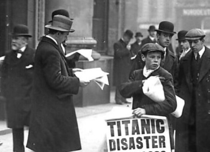 Boy selling newspapers with Titanic disaster headline, surrounded by men in early 20th-century attire in this lesser-known historical photo.