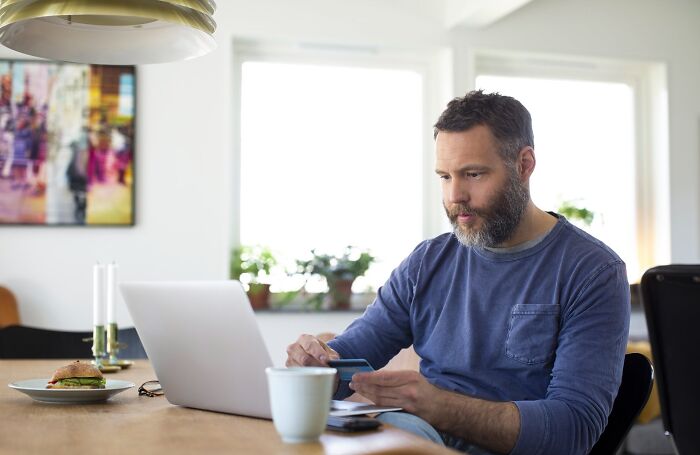 Man using laptop and credit card at home, illustrating consequences of stupidity leading to job loss.