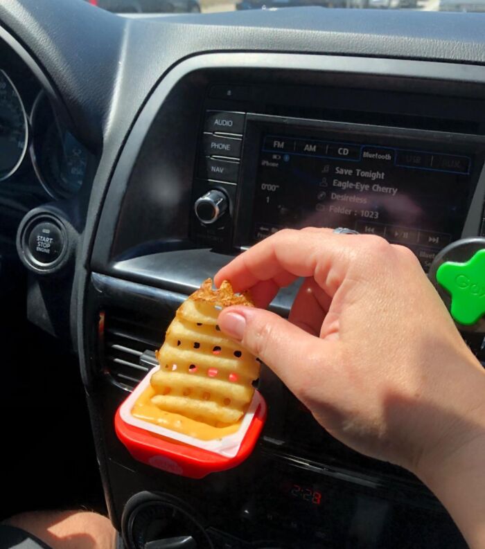 Hand holding waffle fry over dipping sauce attached to car vent, demonstrating car accessories for passenger seat storage unit.