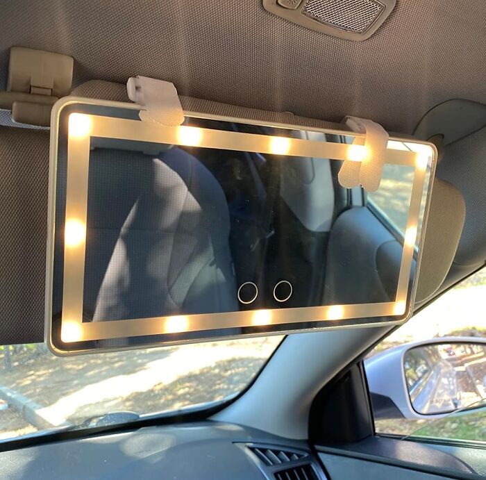 Car accessory vanity mirror with lights attached to car sun visor, ideal for passenger seat storage and convenience.