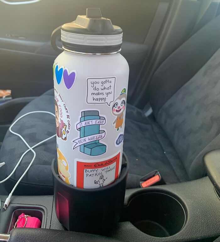 Water bottle with stickers in a car cup holder on passenger seat, showcasing useful car accessories for storage solutions.