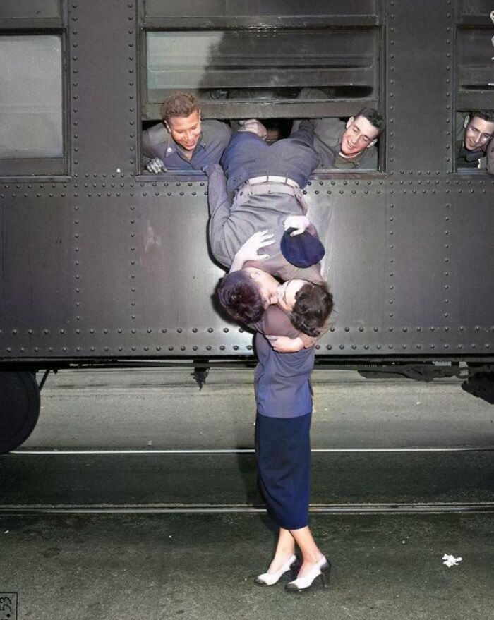 Couple sharing a kiss at a train window, capturing the essence of life in the 1950s with joyful soldiers and onlookers.