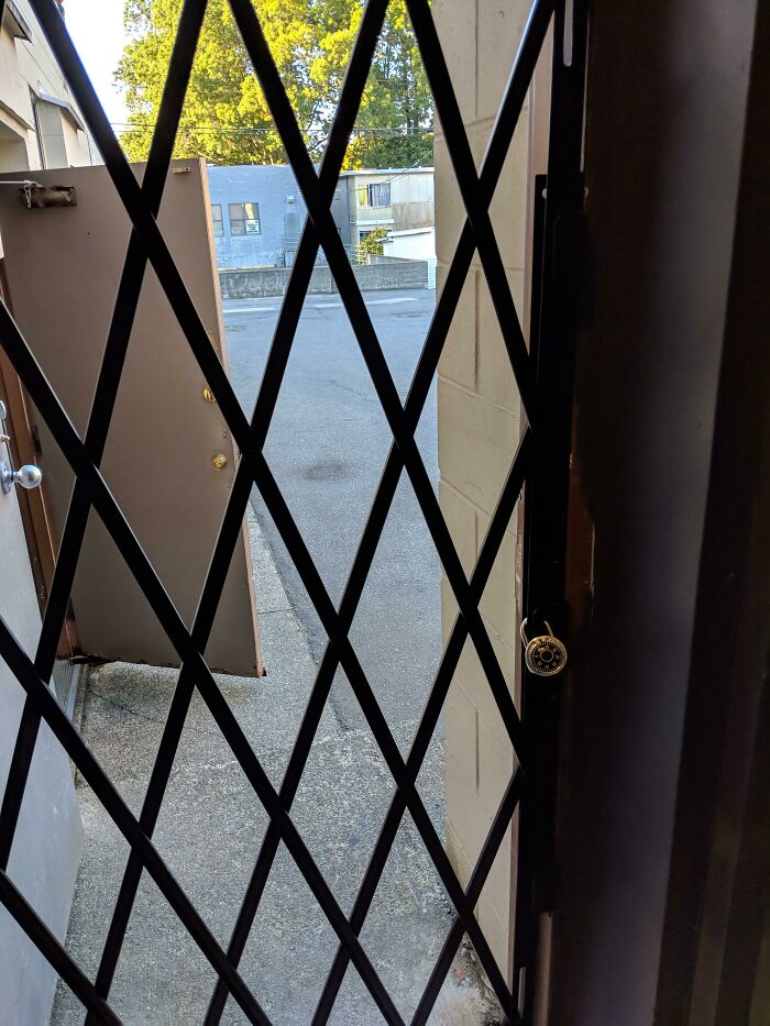 Security gate with a combination lock and an open door showing the outside concrete pathway in a school setting.