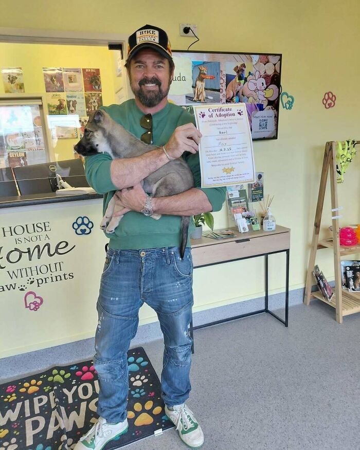 Man holding adopted puppy and certificate of adoption inside a pet adoption center showing happy adopted pets smiling.