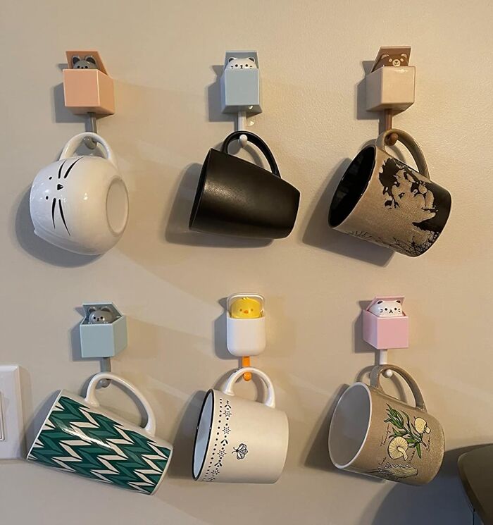 Six quirky mugs hanging on cute animal hooks on a beige wall, showcasing quirky finds for unique home decor.
