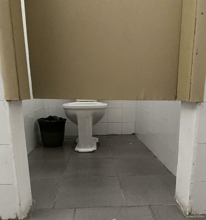 Toilet stall in a school bathroom with a low door and basic facilities, highlighting challenges in some schools' quality.