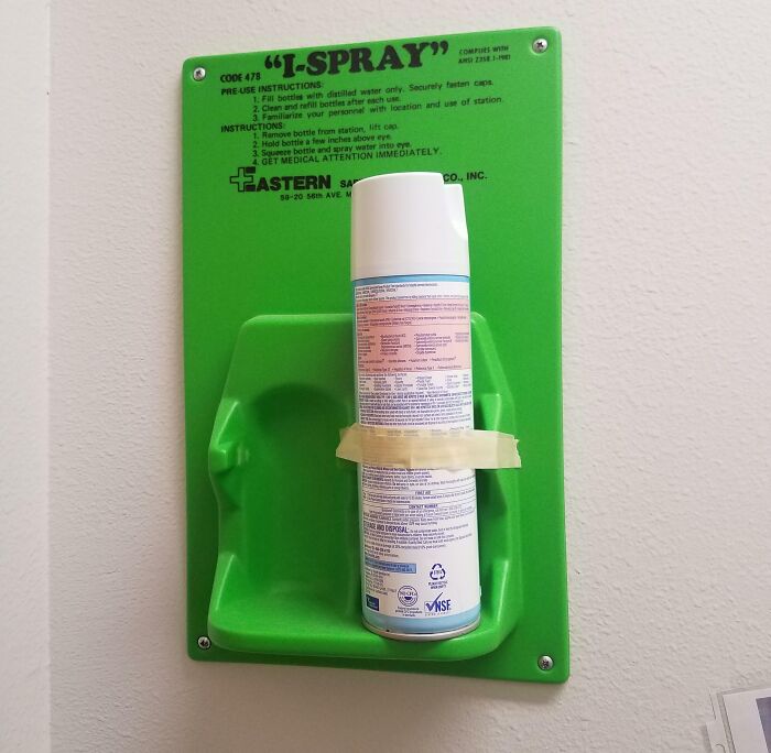 Green emergency spray station in a school bathroom with a can taped in place, highlighting unusual school safety measures.