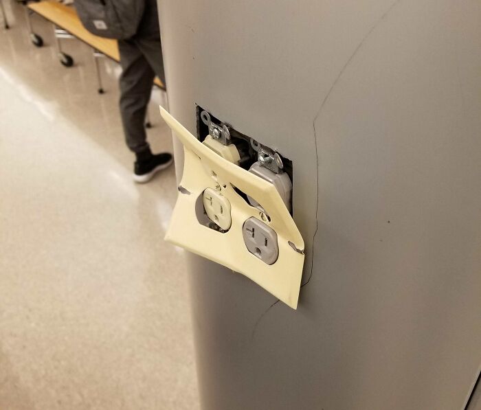 Damaged electrical outlet with c*****d cover on a wall inside a school, highlighting unsafe and unequal school conditions.