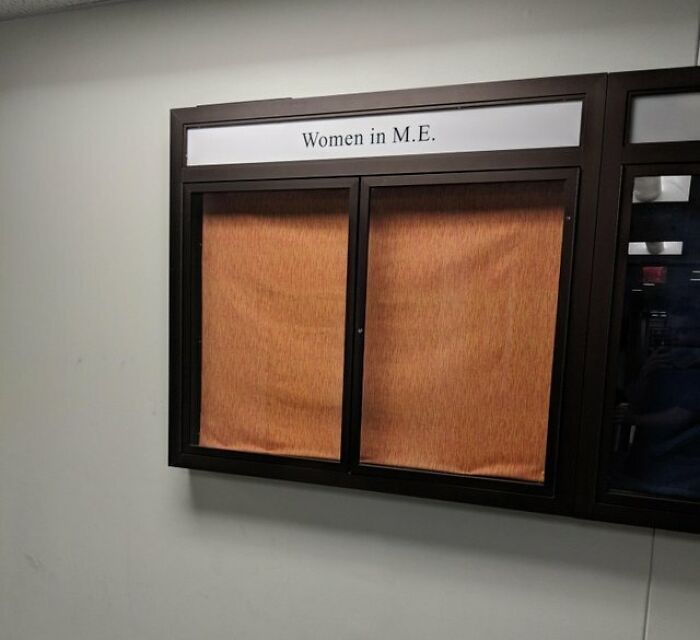 Empty bulletin board labeled Women in M.E. in a school hallway, showing disparity in school recognition and resources.