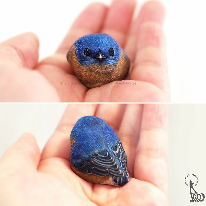 Hand holding a small stone painted by Japanese artist to resemble an adorable blue bird, showcasing detailed animal art.