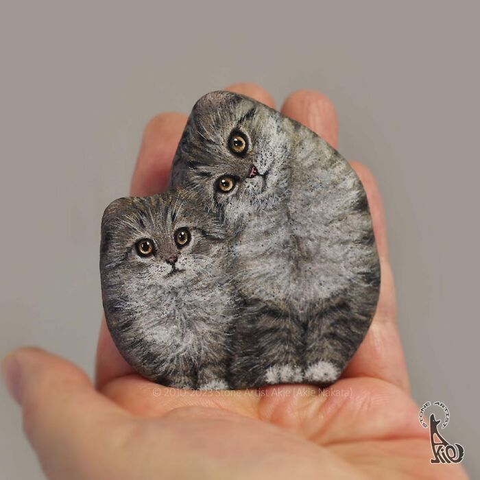 Hand holding a painted stone featuring adorable animals, showcasing Japanese artist's stone art creations.