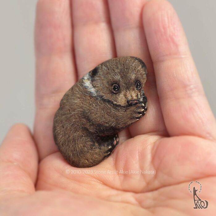 Hand holding a small stone painted by a Japanese artist to look like an adorable realistic animal.