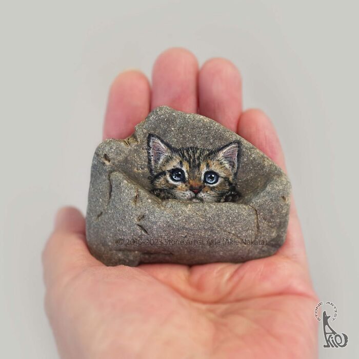 Hand holding a stone painted as an adorable animal, showcasing Japanese artist’s creative stone art.