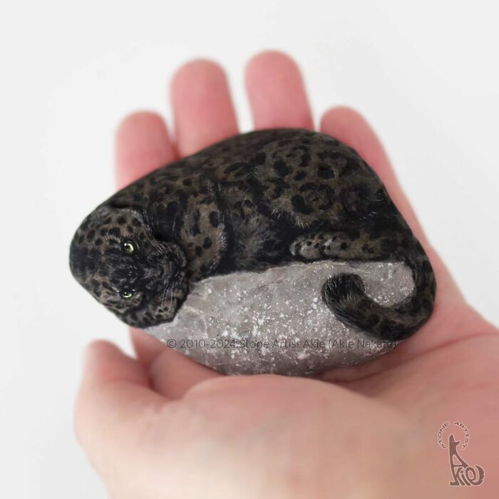 Hand holding a stone painted by Japanese artist to look like an adorable resting leopard animal sculpture.