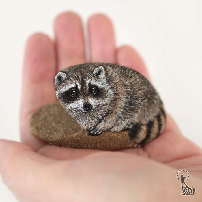 Hand holding a small stone painted by Japanese artist to look like an adorable raccoon animal.