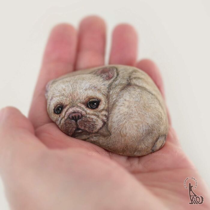 Hand holding a stone painted by a Japanese artist to look like an adorable small curled-up dog.