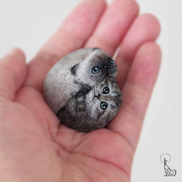 Hand holding a stone painted by Japanese artist to look like two adorable animals with detailed faces.