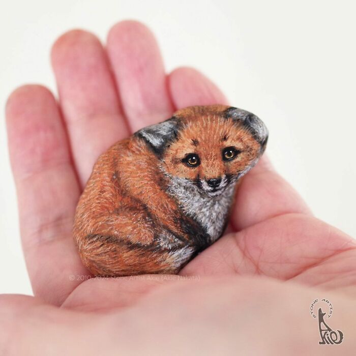 Small stone painted to look like an adorable curled-up fox, showcasing Japanese artist's skill in turning stones into animals.