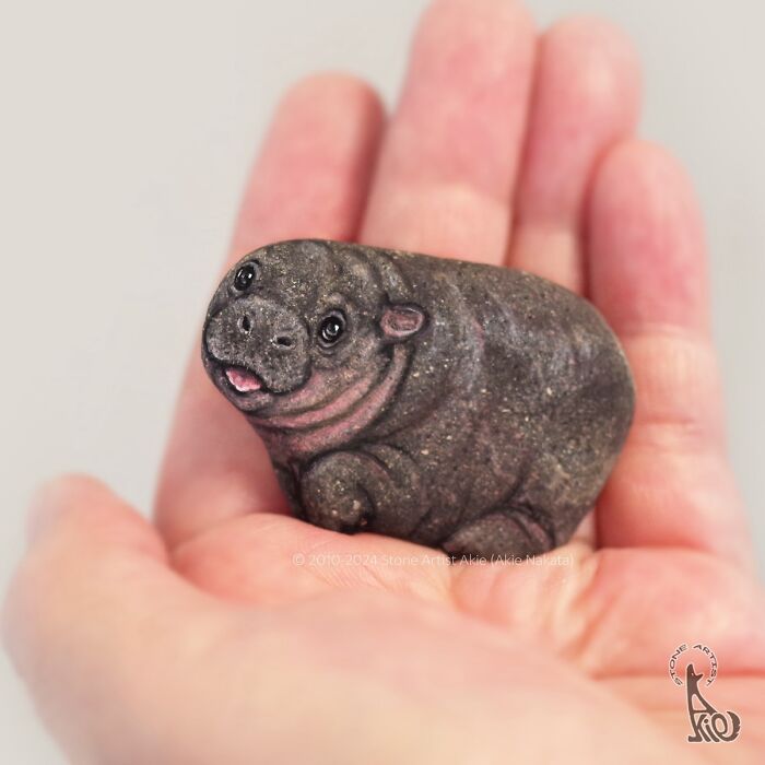 Hand holding a stone painted by Japanese artist to look like an adorable smiling hippo animal sculpture.