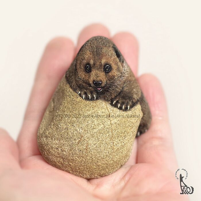Hand holding a small stone painted by a Japanese artist to resemble an adorable animal with detailed eyes and paws.