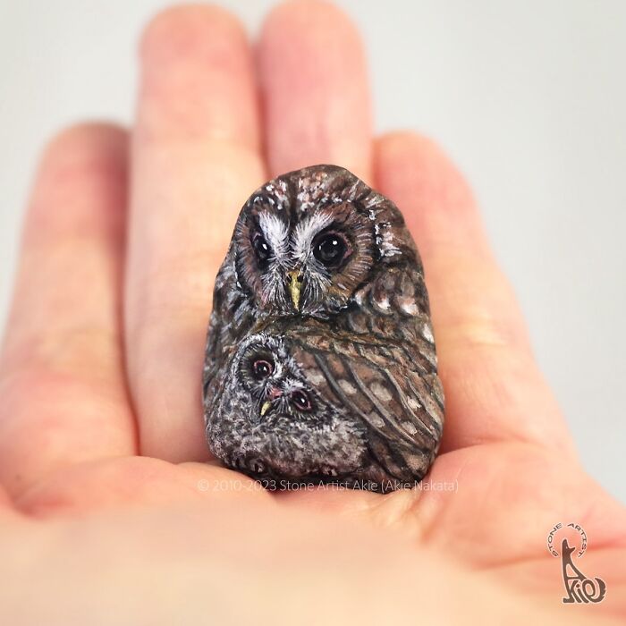 Hand holding a stone painted by Japanese artist featuring two adorable owls as animals in detailed art.