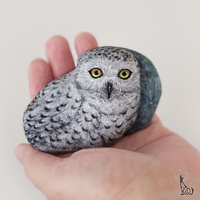 Hand holding a stone painted by Japanese artist to look like an adorable owl animal sculpture.