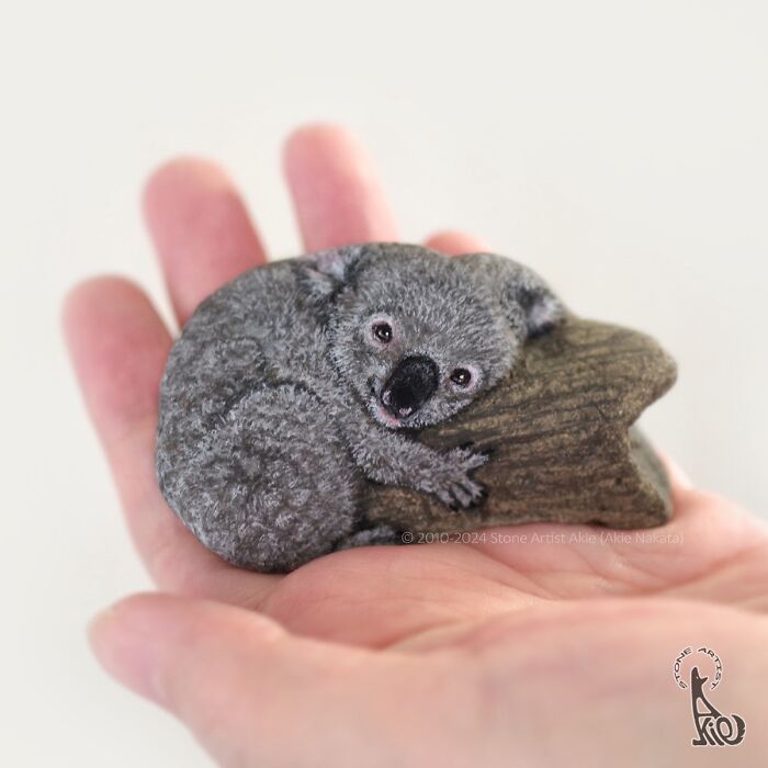 Hand holding a stone painted as an adorable koala, showcasing Japanese artist's skill turning stones into cute animals.