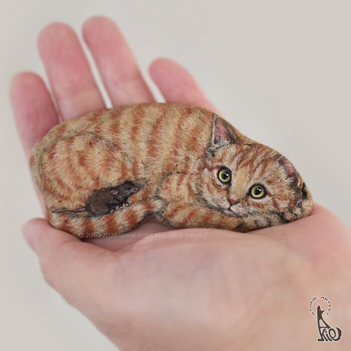 Hand holding a painted stone resembling an adorable striped cat and mouse, showing Japanese artist stone animal art.
