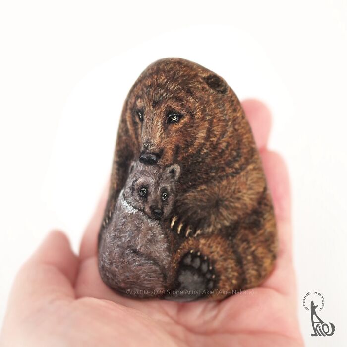 Hand holding a stone painted by Japanese artist with detailed adorable animals, a bear and its cub.