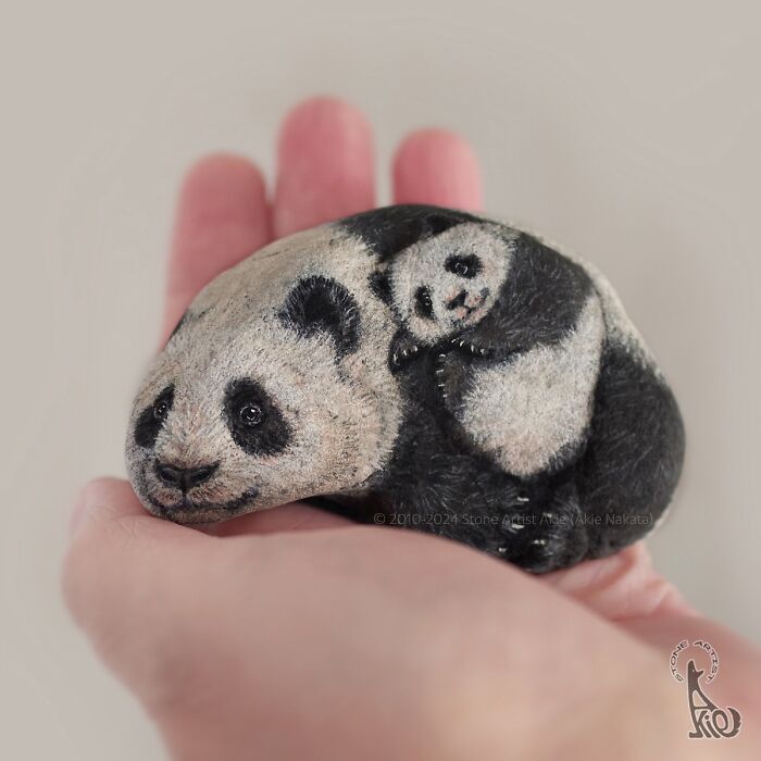 Hand holding a stone painted by a Japanese artist to resemble adorable panda animals with detailed features.