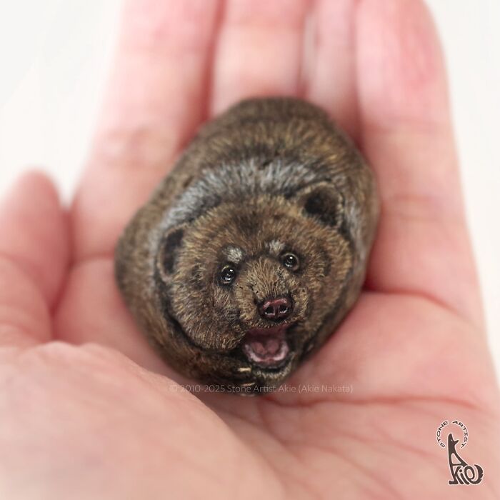 Hand holding a small stone painted by Japanese artist to look like an adorable animal with realistic fur and eyes.