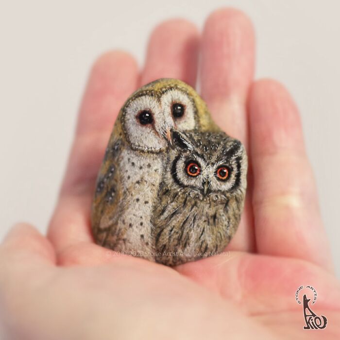 Hand holding a small stone painted by Japanese artist to resemble two adorable owls in detailed animal artwork.