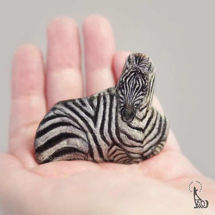 Small stone painted with detailed zebra stripes held in palm, showcasing Japanese artist's adorable animal stone art.
