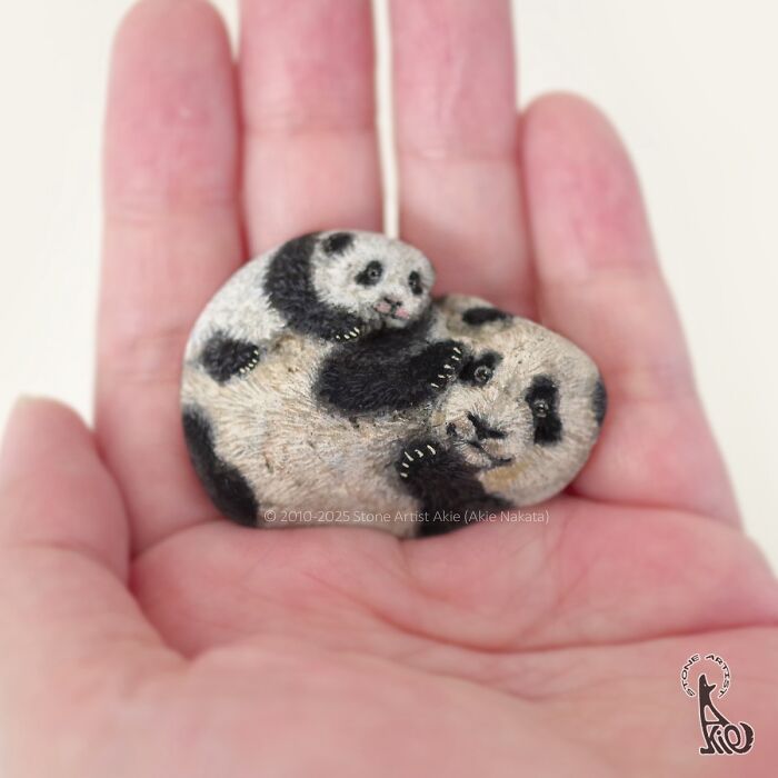 Hand holding a stone painted as adorable animals by Japanese artist, featuring lifelike pandas in a small size.
