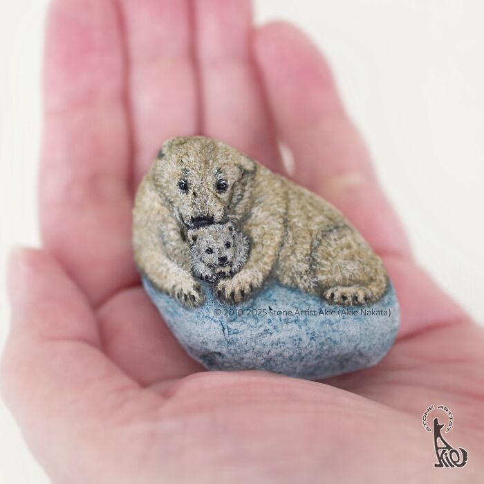 Hand holding a stone painted by Japanese artist featuring adorable animals, a mother bear and cub resting together.