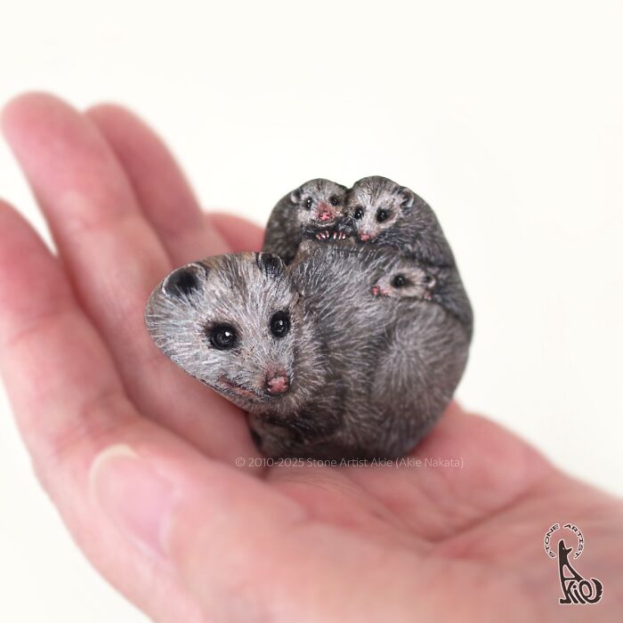 Hand holding a stone painted by Japanese artist to look like a family of adorable small animals with detailed fur.