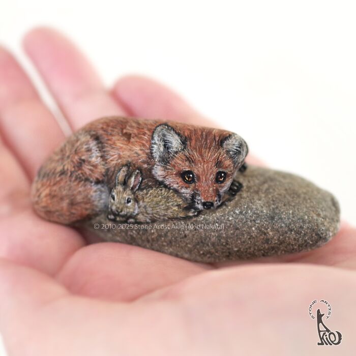 Hand holding a painted stone transformed into an adorable fox and rabbit, showcasing Japanese artist’s animal creations.