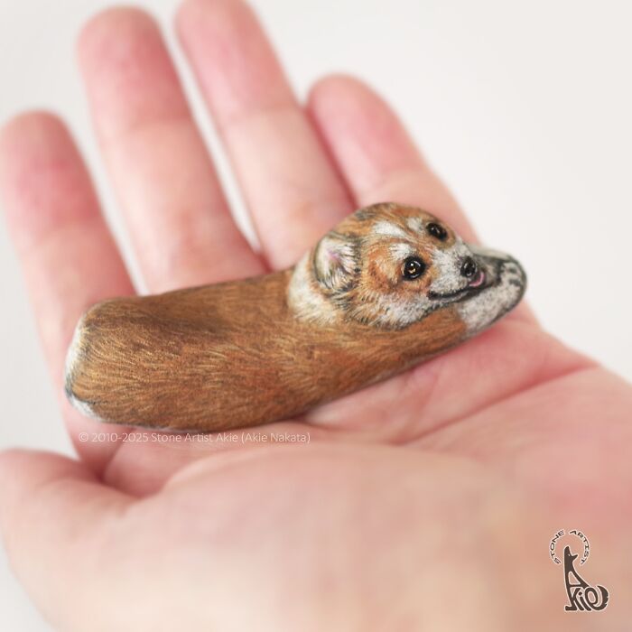 Small stone painted by Japanese artist to look like an adorable resting animal, held gently in a hand.