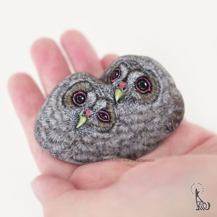 Hand holding stone painted by Japanese artist featuring two adorable owls with detailed eyes and feathers.