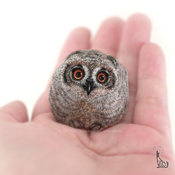 Hand holding a small stone painted by Japanese artist to resemble an adorable owl with detailed eyes and feathers.