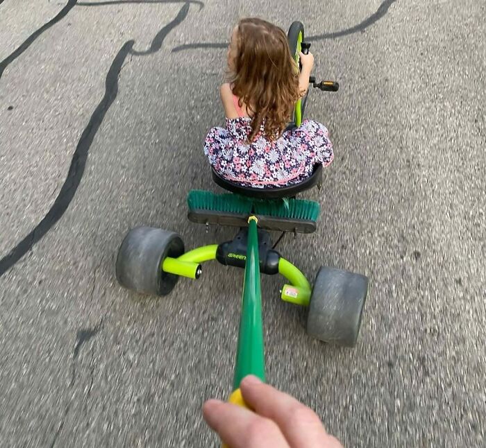 Dad creatively uses a broom attached to a tricycle to pull a young girl, showcasing hilarious dad moments in fatherhood.